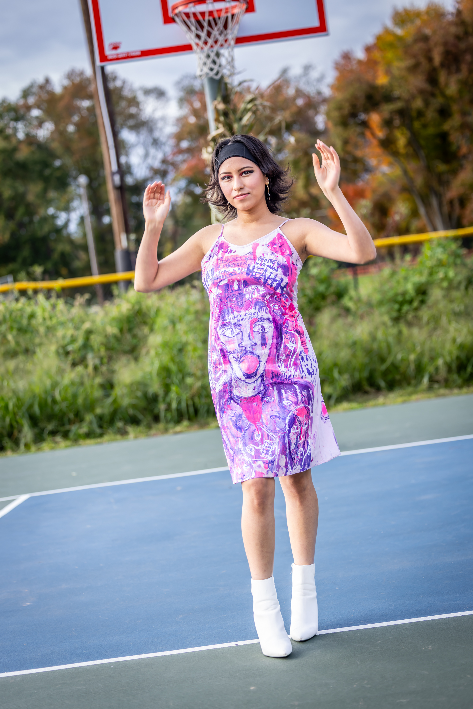 Model posing on basketball court in hand-painted pink and purple dress with white boots