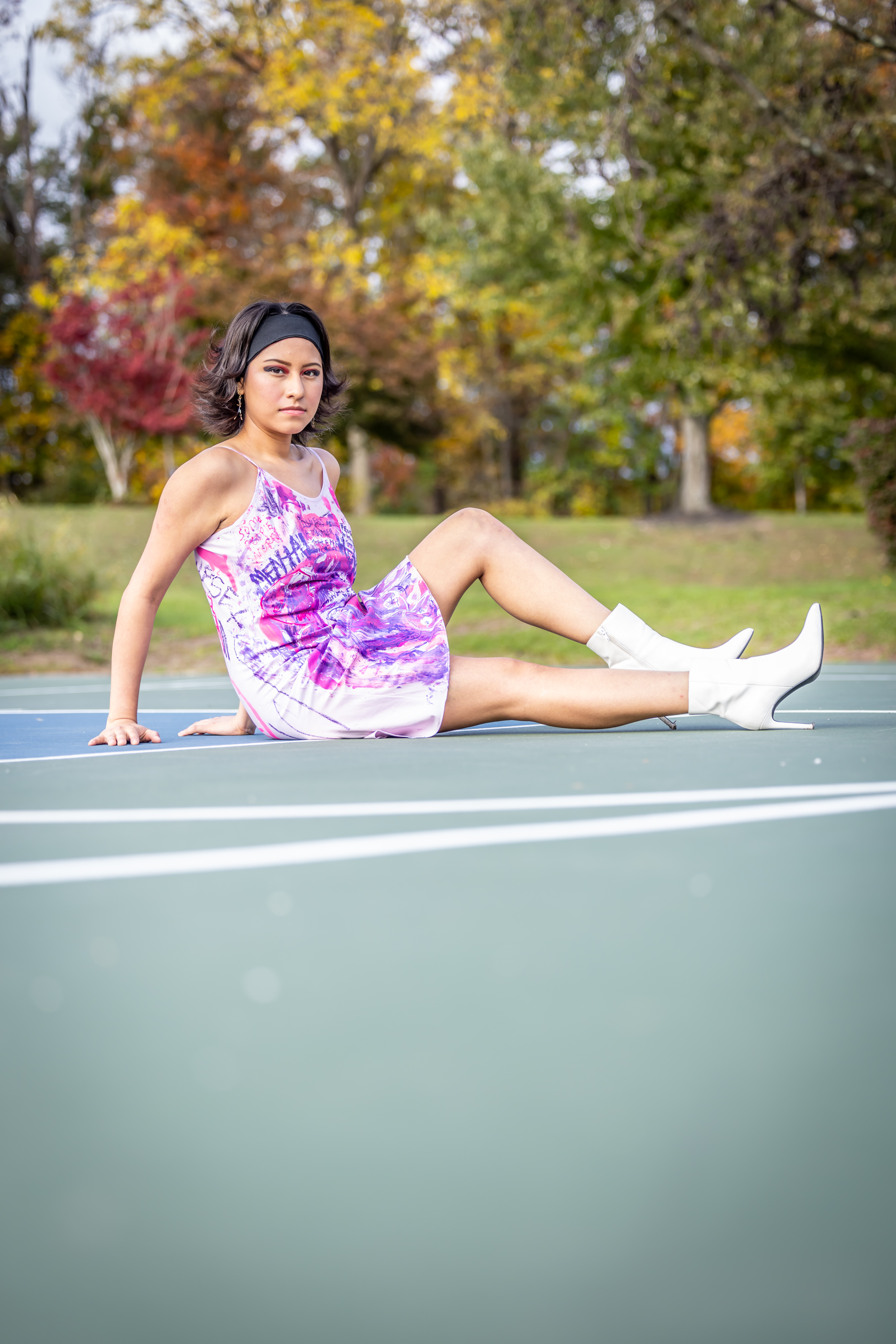 Model sitting on tennis court in hand-painted purple dress with white heeled boots